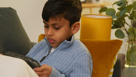 Young-Boy-Sitting-On-Sofa-At-Home-Playing-Game-Or-Streaming-Onto-Handheld-Gaming-Device-4